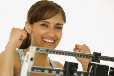 Young woman standing on a weighing scale with arms raised in excitement