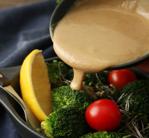 Close up of citrus tahini salad dressing being poured over blanched broccoli and  cherry tomatoes